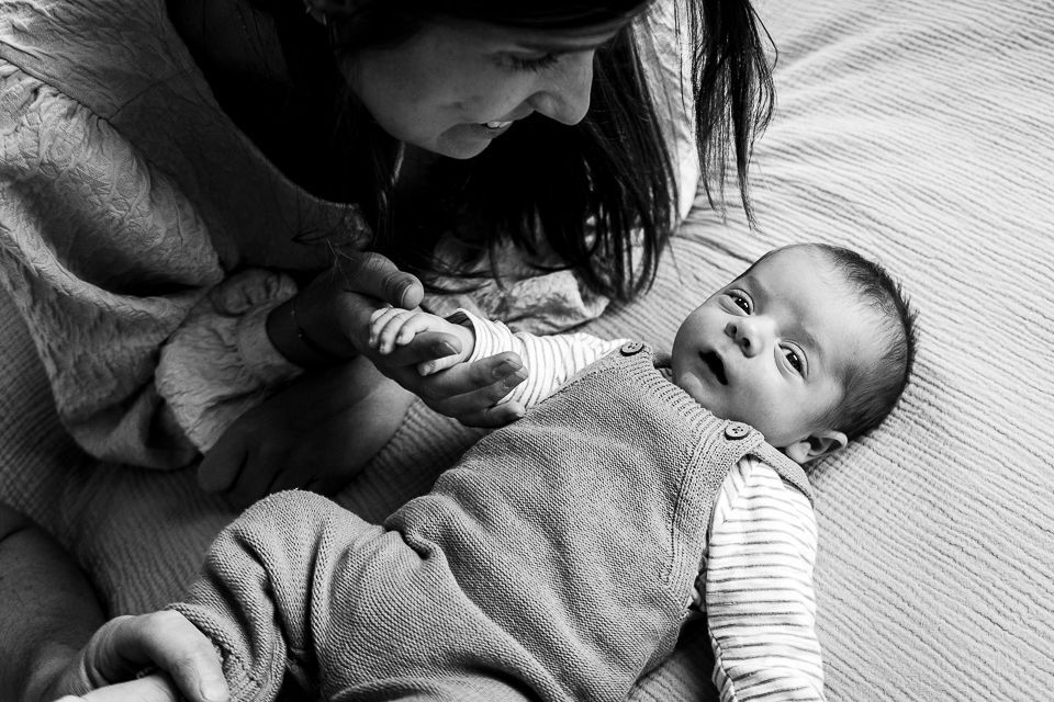 Een vrouw kijkt naar een baby in een overall; ze houdt voorzichtig het handje van de baby vast.