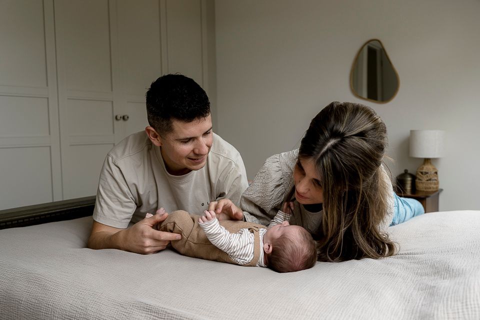 Ouders kijken naar hun pasgeboren baby die op een bed ligt.