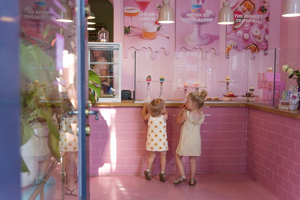 Twee jonge kinderen kijken naar een roze ijssalon, met op de achtergrond een blauwe deuropening en raamreflectie.