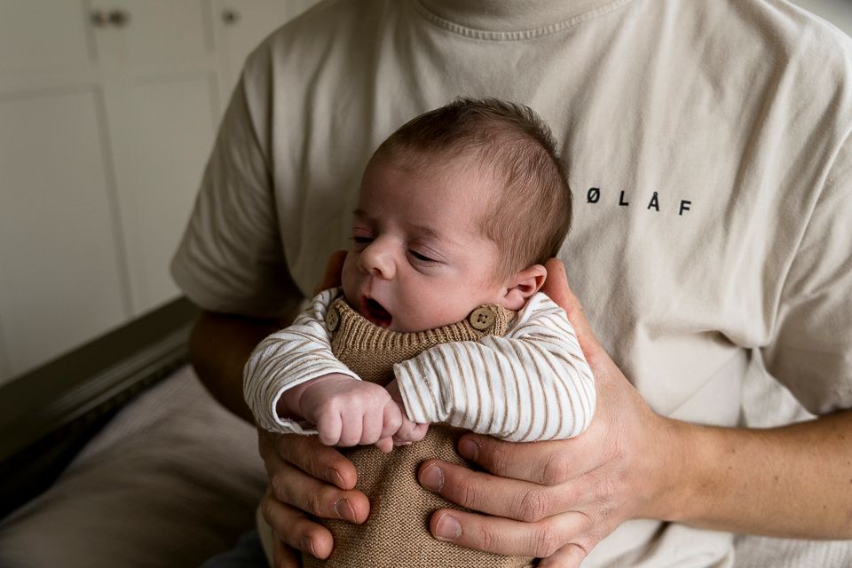Pasgeboren baby, gekleed in een beige outfit, met gesloten ogen, wordt in de armen gehouden.