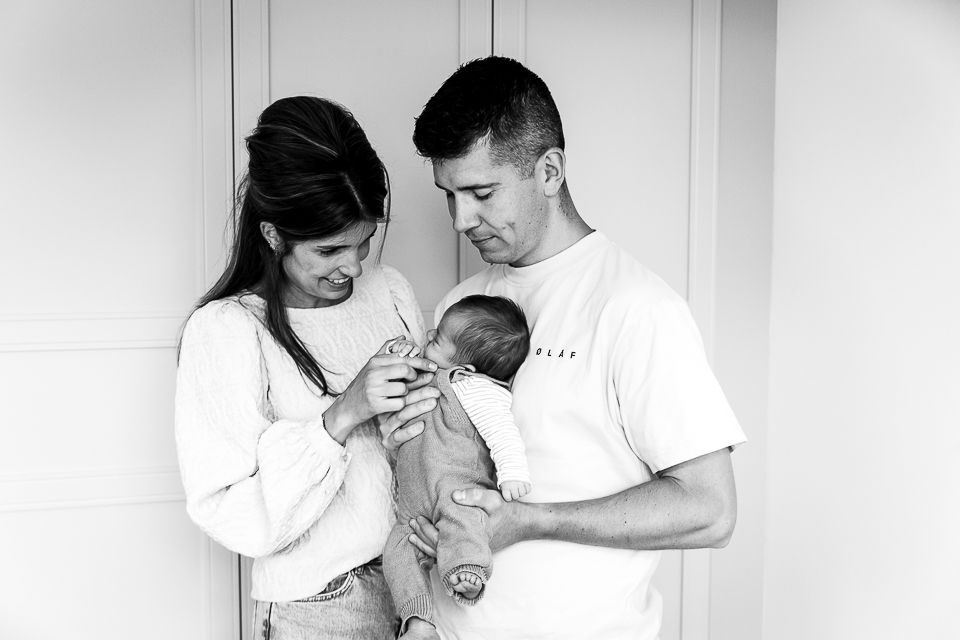 Ouders houden een pasgeboren baby vast en kijken ernaar, poserend voor witte deuren.
