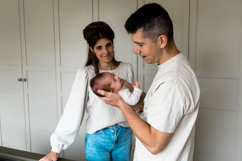 Ouders houden een pasgeboren baby vast en glimlachen. Neutrale omgeving, lichte kleding, helder licht.