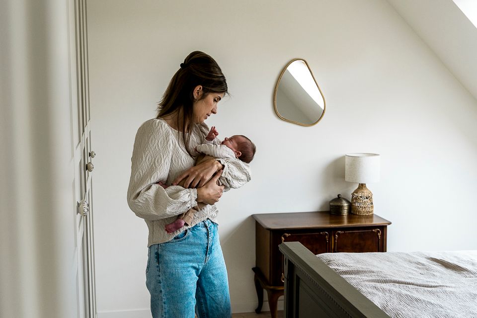 Vrouw houdt een baby vast in een lichte slaapkamer en kijkt naar het kind.