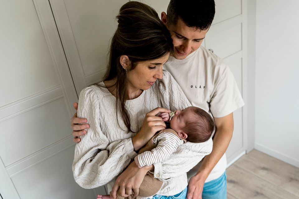 Ouders houden een pasgeboren baby vast en kijken ernaar. De kamer is wit.