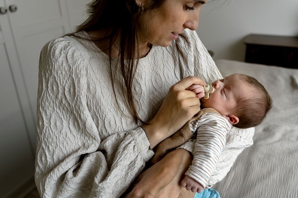 Vrouw houdt een baby vast en geeft hem de fles met een fopspeen binnenshuis.