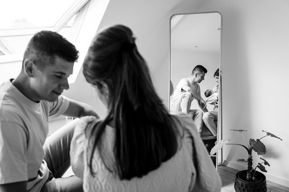Een stel kijkt in een spiegel. De spiegel reflecteert een man, een kind en een vrouw in een lichte kamer.