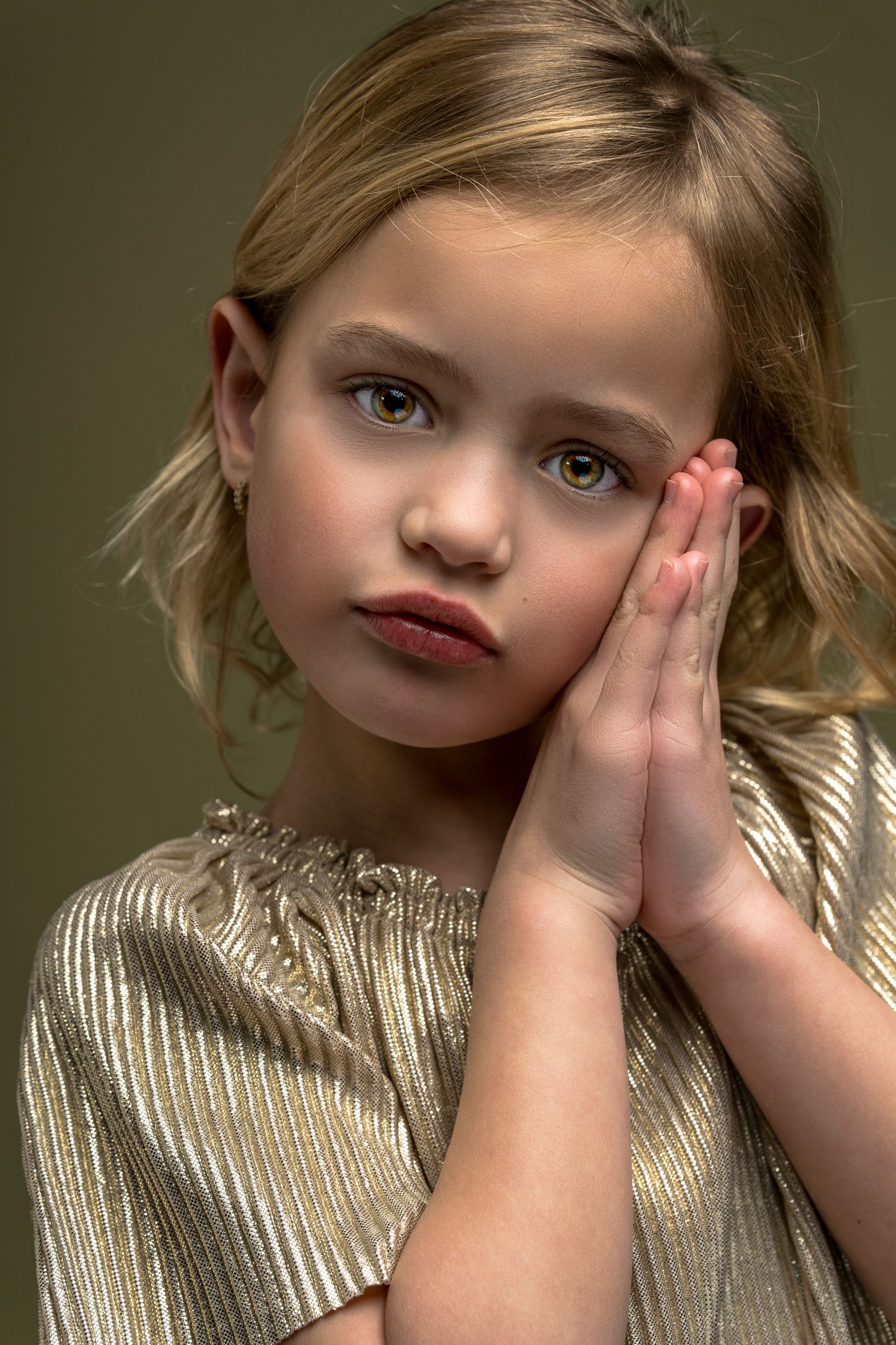 Meisje in gouden top, met haar hoofd in haar handen, kijkt naar de kijker.