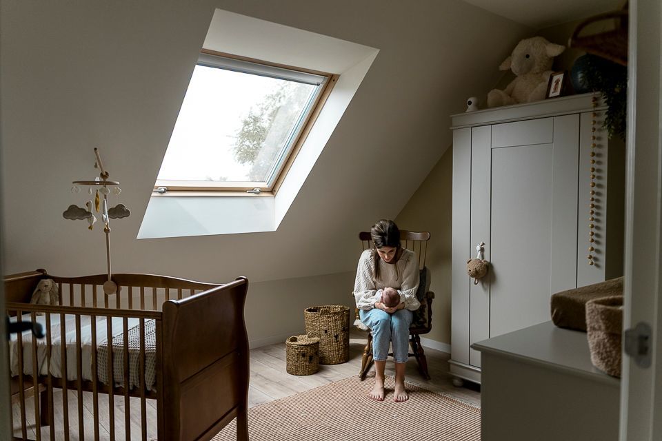 Vrouw met een baby in een kinderkamer met een wieg, kast en dakraam.
