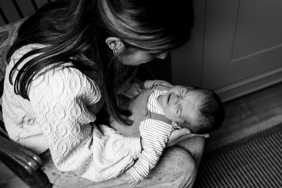 Vrouw houdt een pasgeboren baby op haar schoot en kijkt glimlachend naar de baby. Zwart-witfoto.
