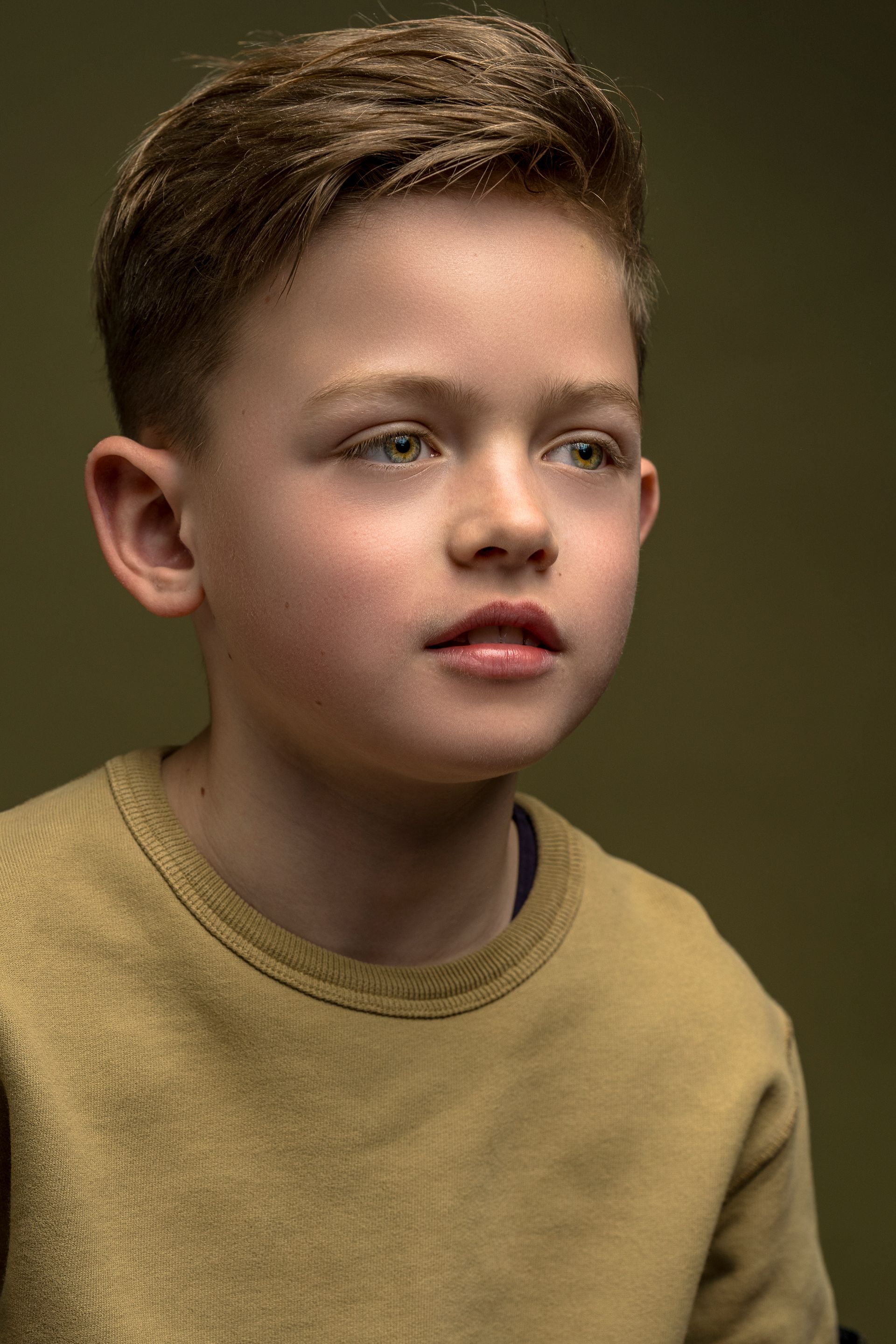 Een jong persoon met licht haar en een lichte huid kijkt iets opzij. Hij draagt een geel shirt.