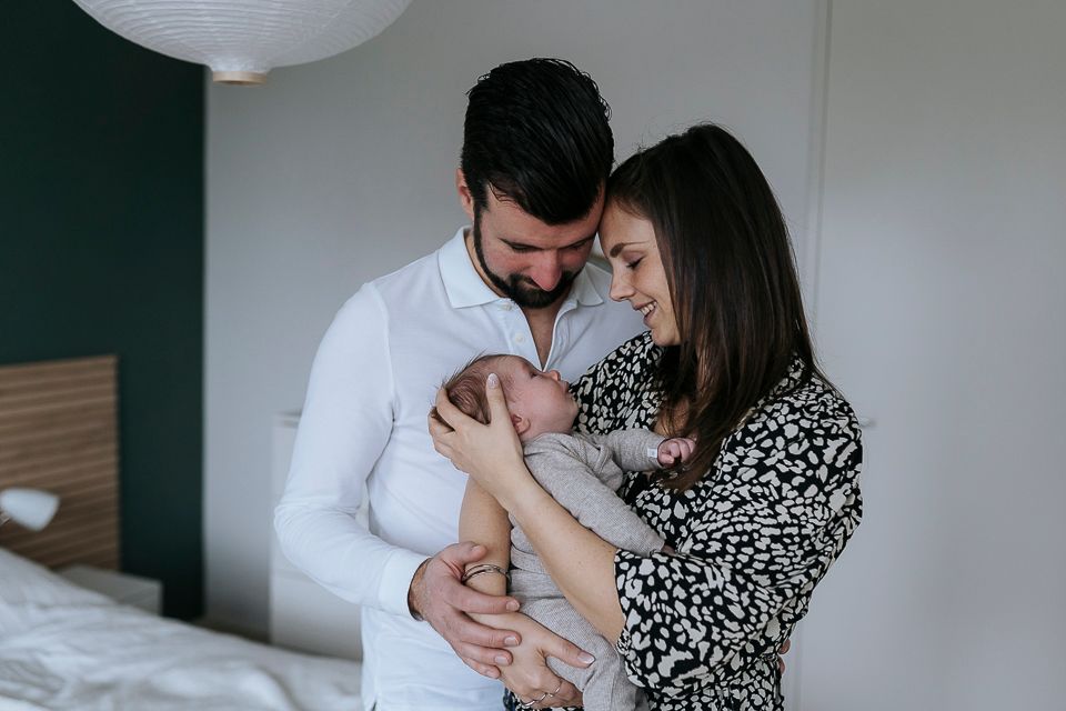 Ouders kijken naar hun pasgeboren baby. Moeder houdt de baby vast, vader kijkt naar beneden, slaapkameromgeving.