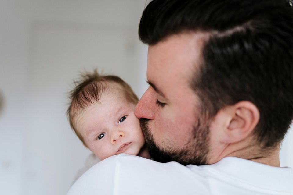 Een man kust een pasgeboren baby op de wang; de baby kijkt naar de camera.