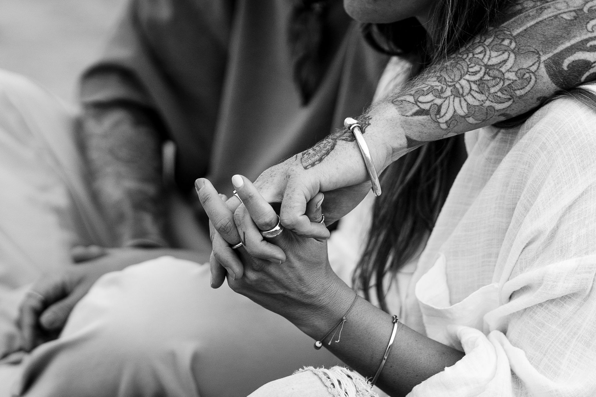 Twee mensen houden elkaars hand vast, één arm is getatoeëerd, in zwart-wit.