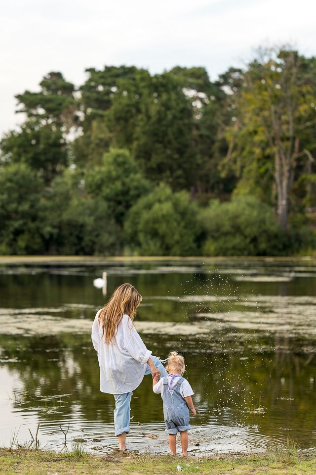 Vrouw en kind staan ​​aan de rand van een meer en spetteren in het water. Groene bomen op de achtergrond.