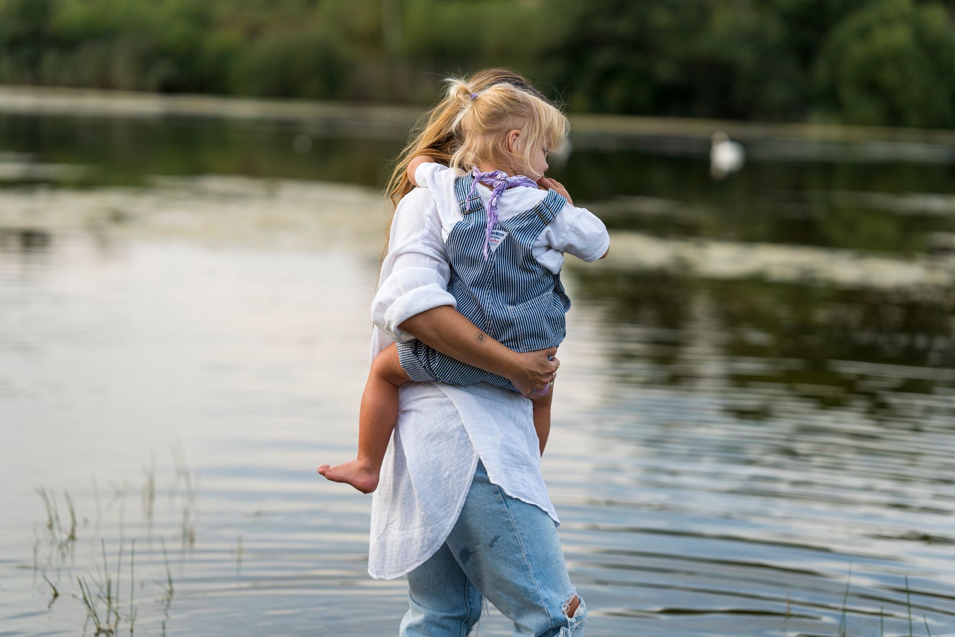 Een vrouw houdt een kind vast bij een meer. Beiden kijken weg.