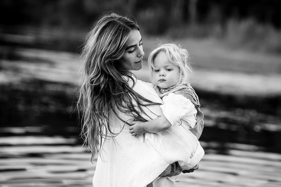 Vrouw die een kind in het water vasthoudt; beiden kijken naar het kind, zwart en wit.