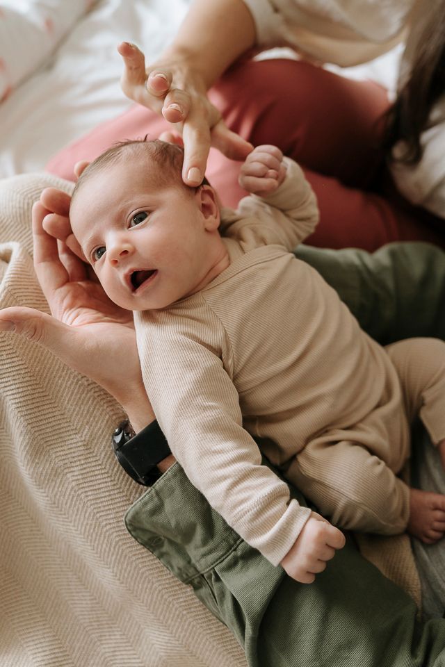 Pasgeboren baby in beige rompertje wordt in de armen gehouden, iemand raakt het hoofdje aan.