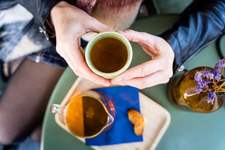 Vrouw met een kop thee in haar hand, met een theepot en bloemen op een tafel.