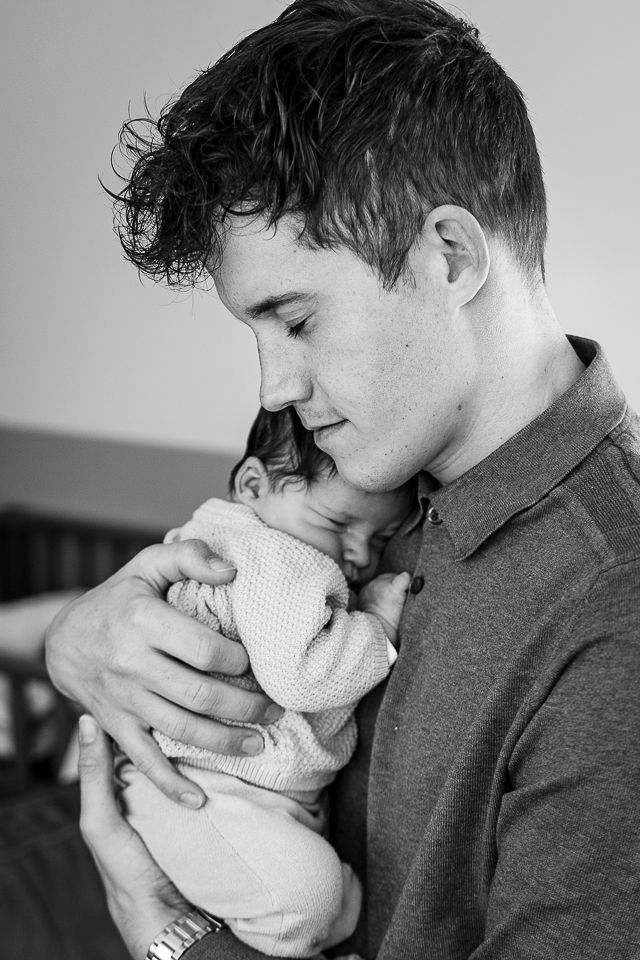 Man die een slapende baby dicht tegen zijn borst houdt; zwart-wit.