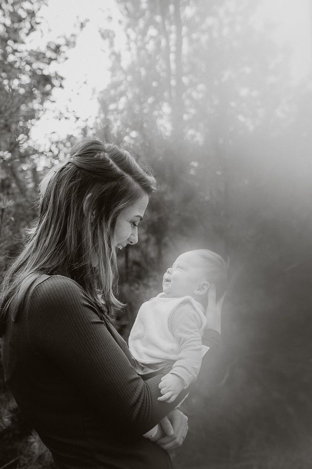 Vrouw houdt een baby vast en kijkt ernaar. Buiten, bomen op de achtergrond, grijstinten.