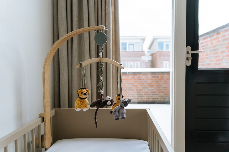 Houten wieg met een hangende mobiel met dierenfiguurtjes; raam op de achtergrond.