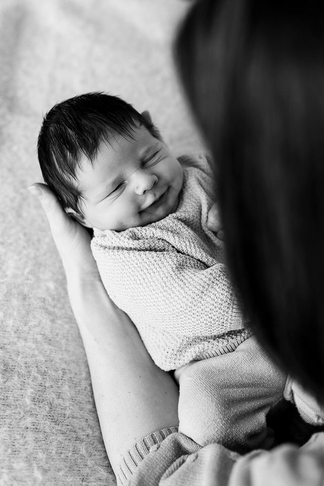Pasgeboren baby, gewikkeld in een deken, lacht en wordt in de armen gehouden.