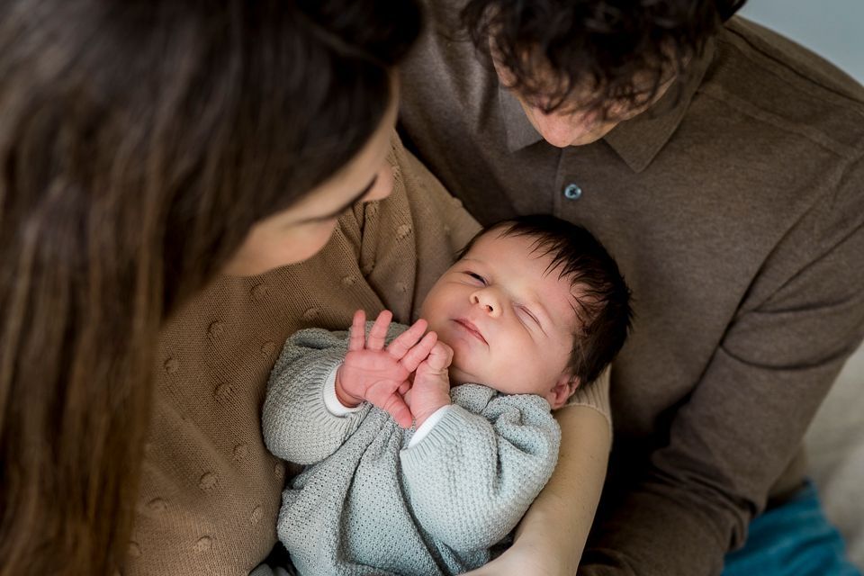 Ouders houden een pasgeboren baby vast. De baby draagt ​​een lichtblauw truitje en heeft zijn ogen gesloten.