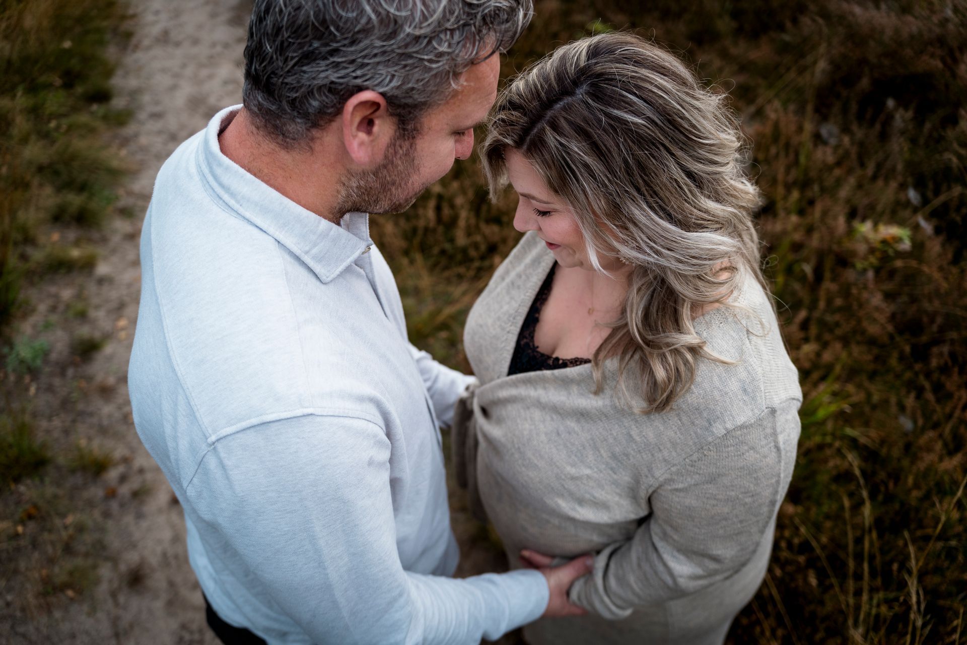 Een man en een zwangere vrouw, buiten. De man raakt zachtjes de buik van de vrouw aan. Beiden kijken naar beneden en glimlachen.