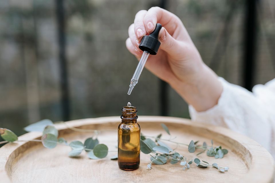 Hand die een pipet vasthoudt waarmee vloeistof in een amberkleurige fles op een houten dienblad met groen wordt gedoseerd.