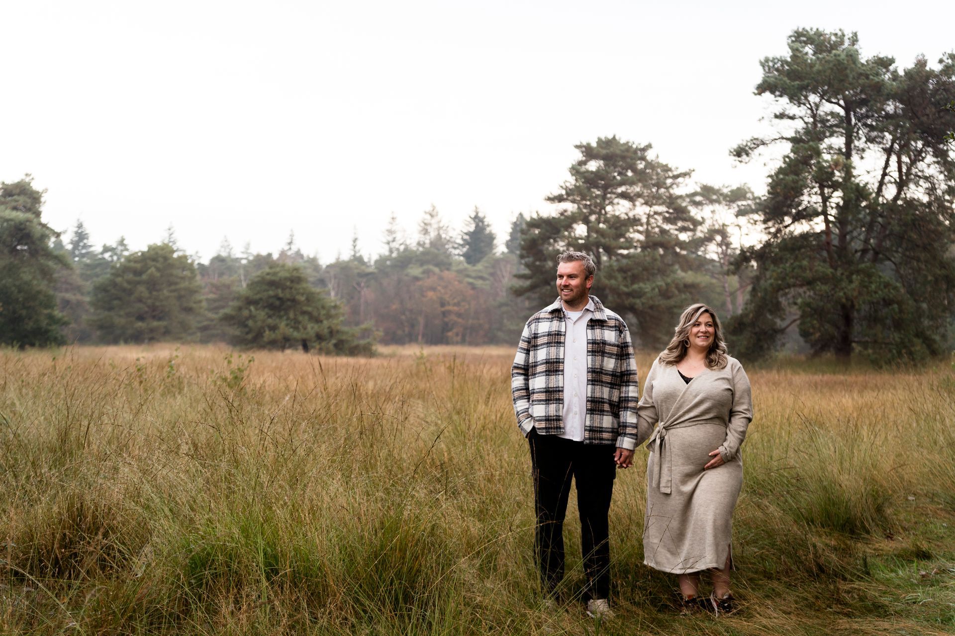 Een stel loopt hand in hand in een grasveld; de man draagt ​​een geruit overhemd, de vrouw een crèmekleurige jurk. Op de achtergrond is een bos te zien.