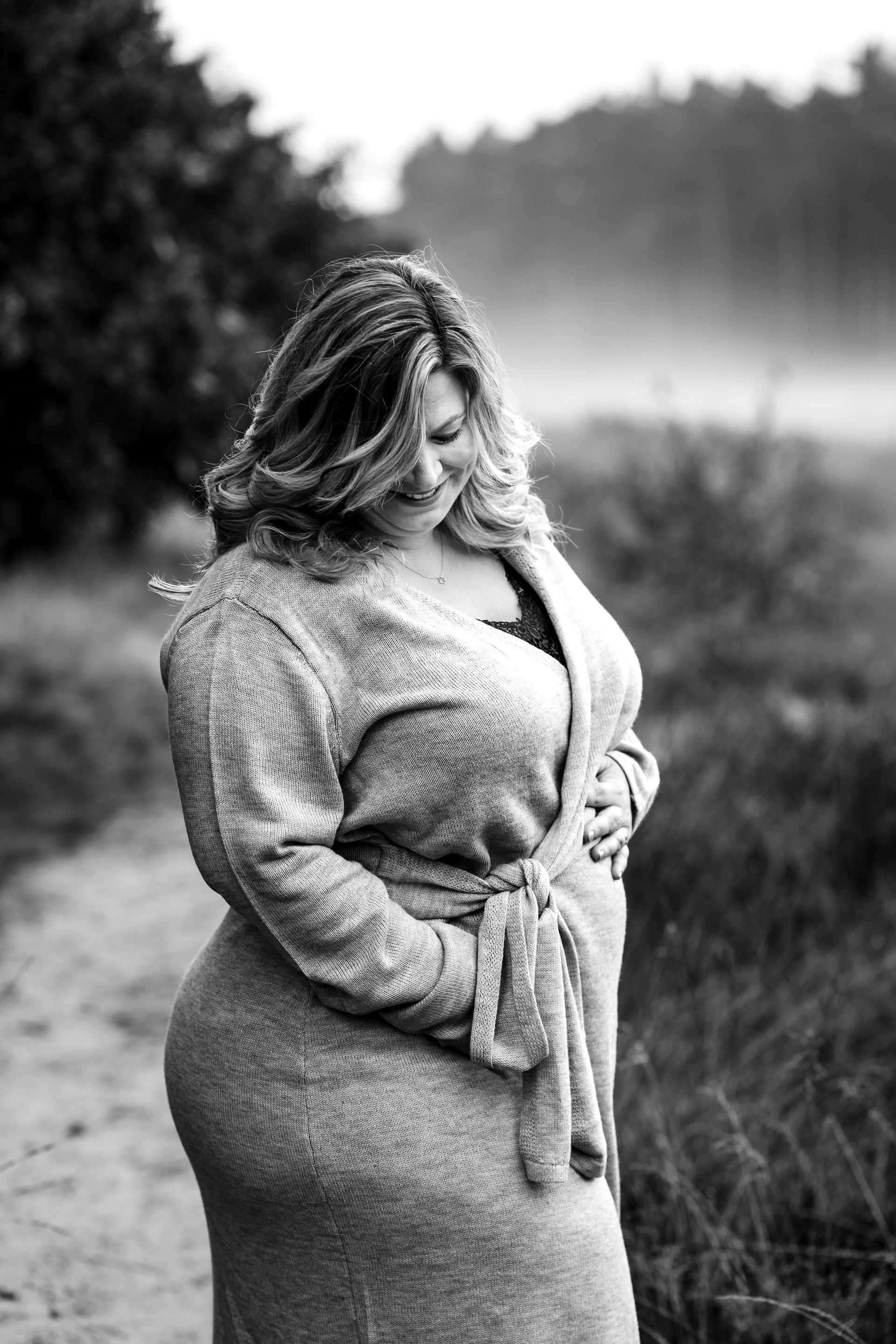 Zwangere vrouw, buiten. Handen rusten zachtjes op haar buik. Draagt ​​een vest.