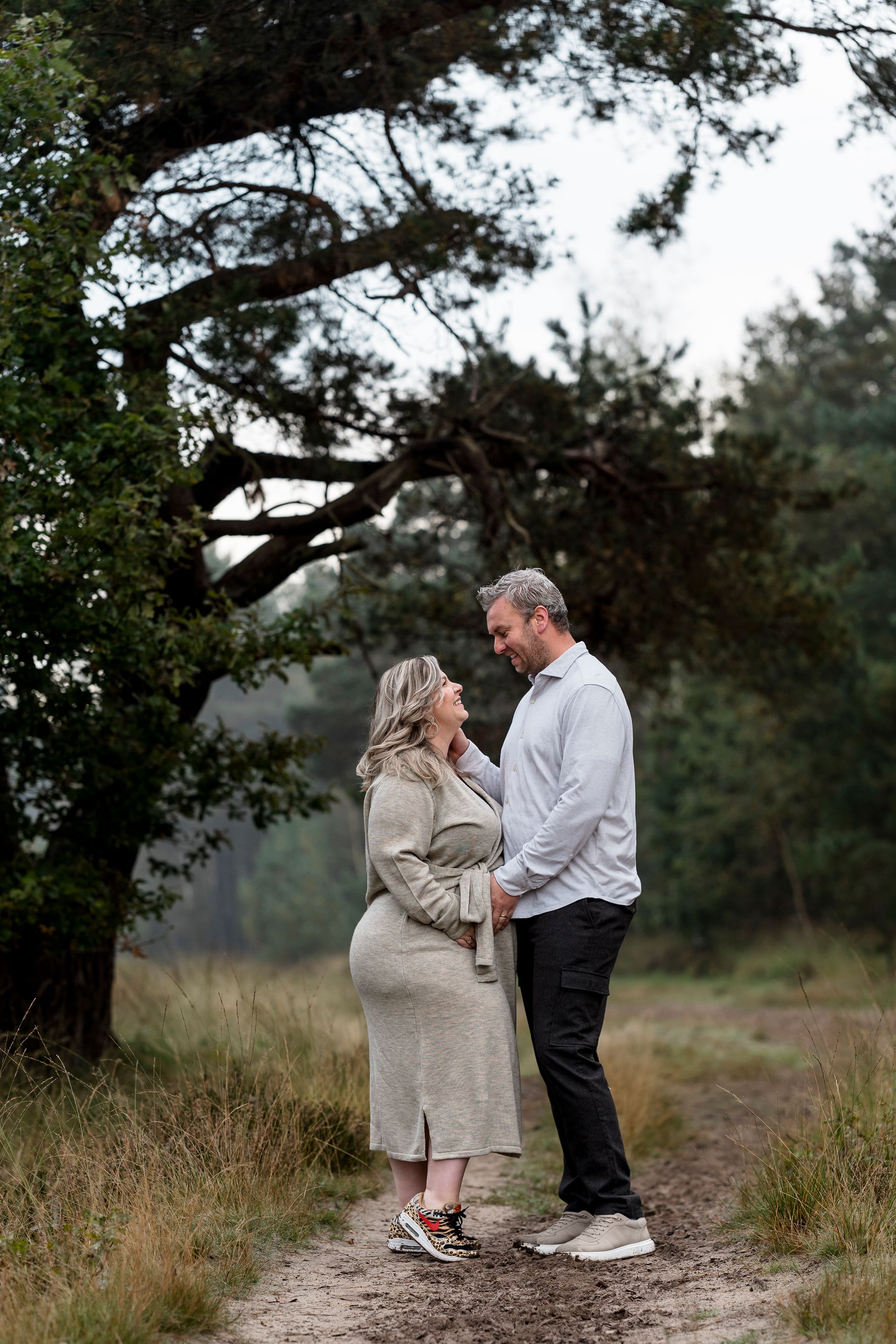 Een stel kijkt elkaar aan op een pad in het bos. De vrouw draagt ​​een jurk met een patroon, de man een overhemd.