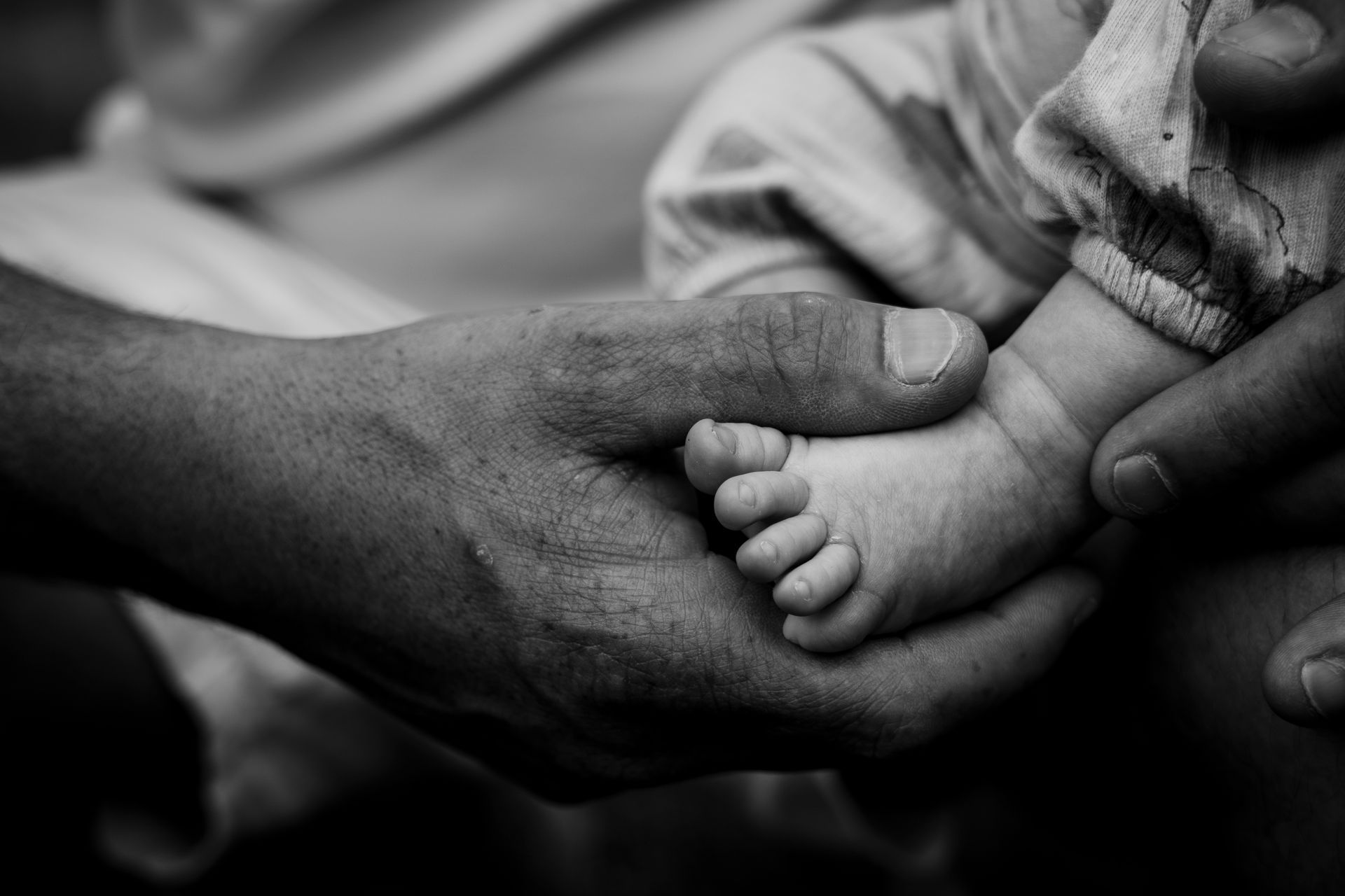 De handen van een volwassene omvatten het kleine voetje van een baby, zwart-witfoto.