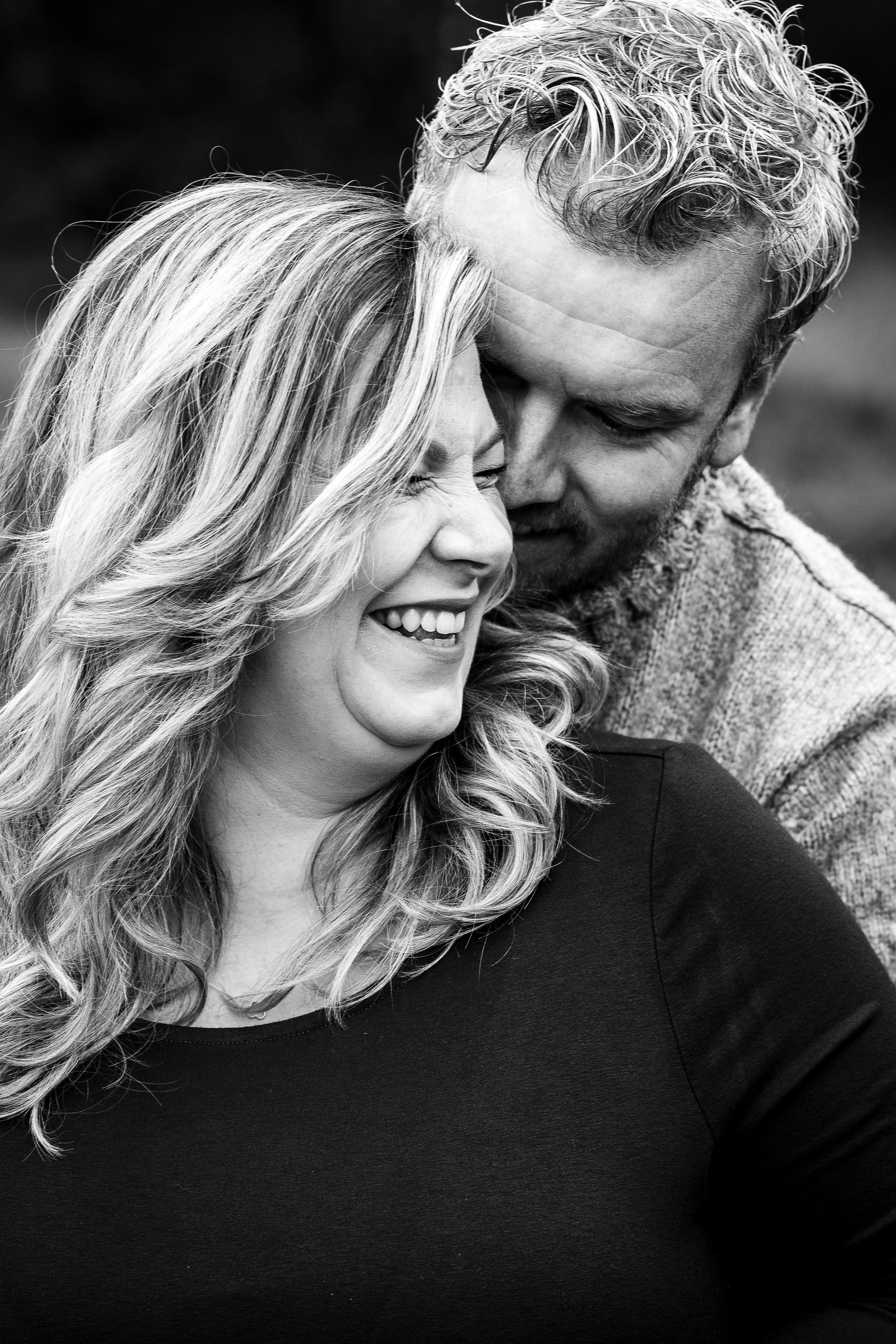 Vrouw lacht terwijl een man haar omhelst, buiten. Zwart-witfoto.