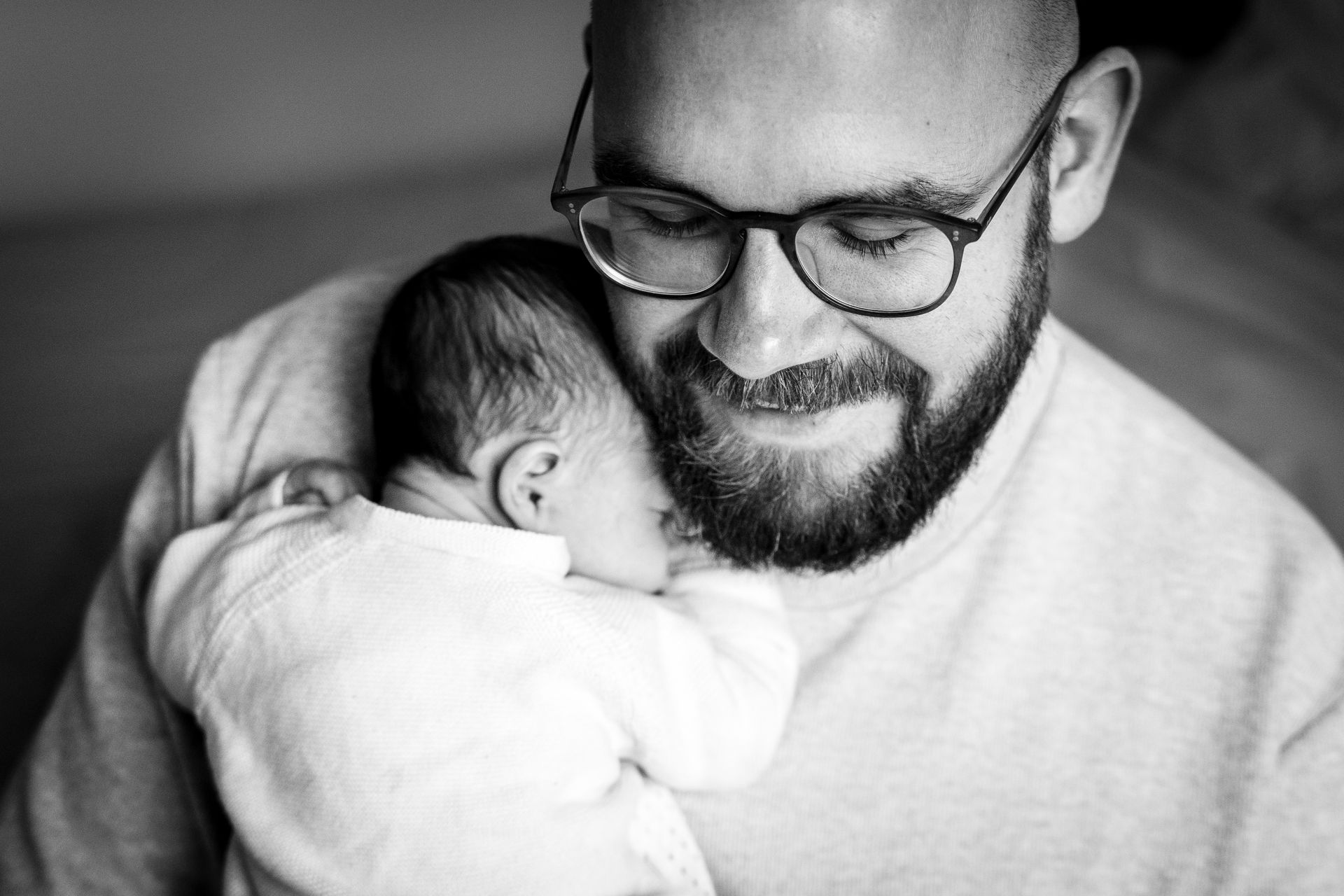 Een man met een bril en een baard houdt een slapende baby dicht tegen zijn borst.