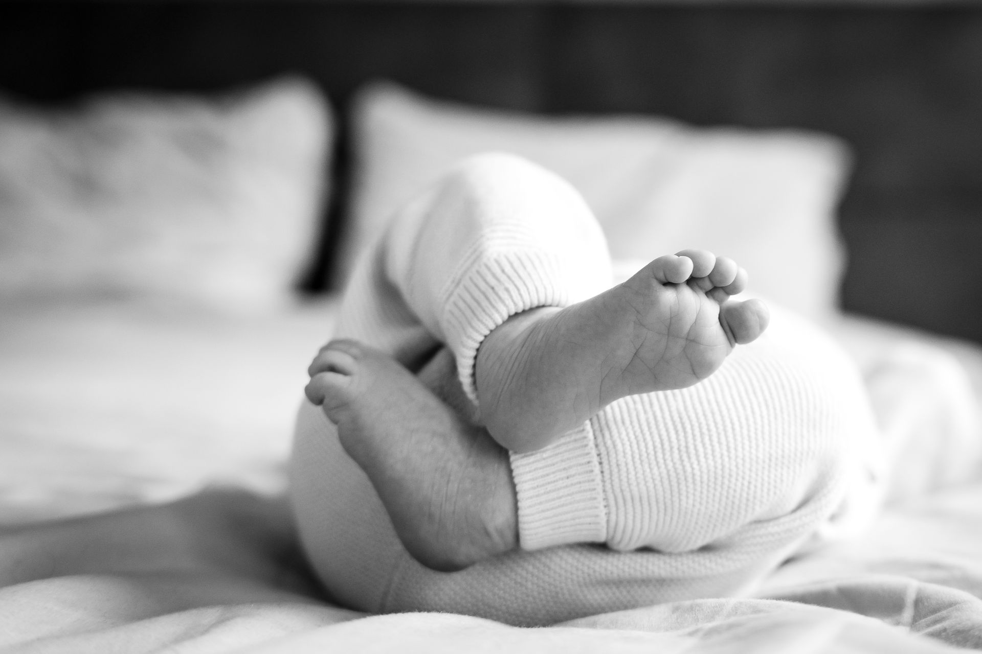 Babyvoetjes en -beentjes in een wit rompertje op bed; zwart-witfoto.