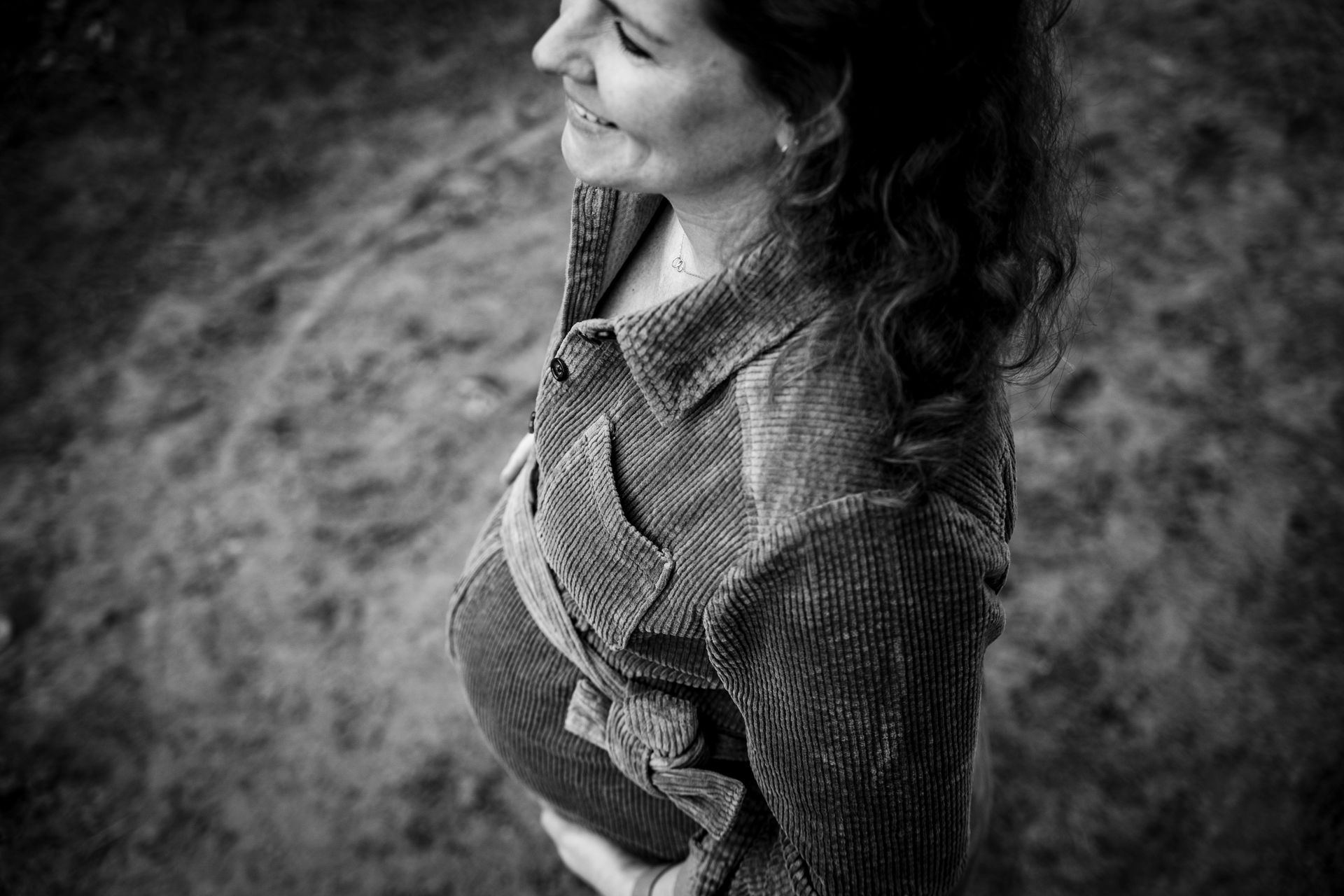 Zwangere vrouw, lachend, haar buik vasthoudend, corduroy shirt dragend, buiten.