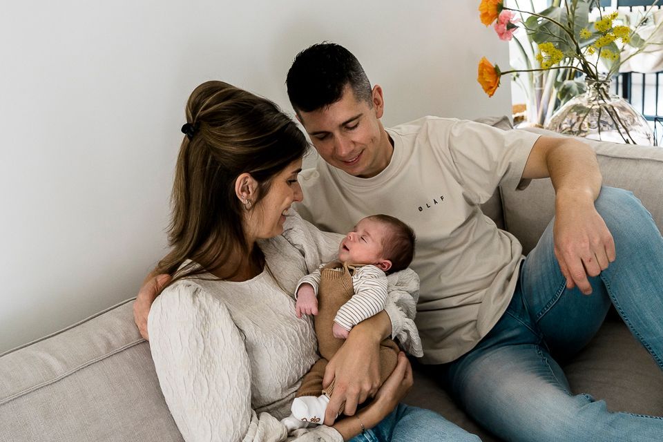 Ouders op de bank met een pasgeboren baby. De ouders glimlachen. De baby is ingewikkeld en slaapt.