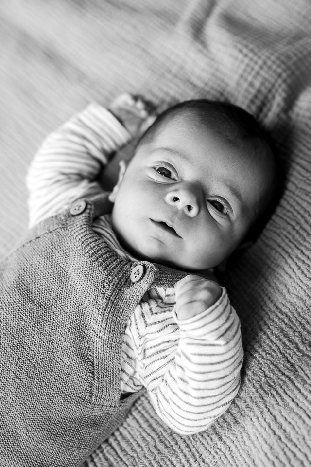 Pasgeboren baby in gestreept shirt en gebreide overall kijkt naar de camera. Zwart-wit.