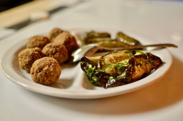 Piatto bianco con antipasti fritti, pesce in salsa e un cucchiaio su un tavolo