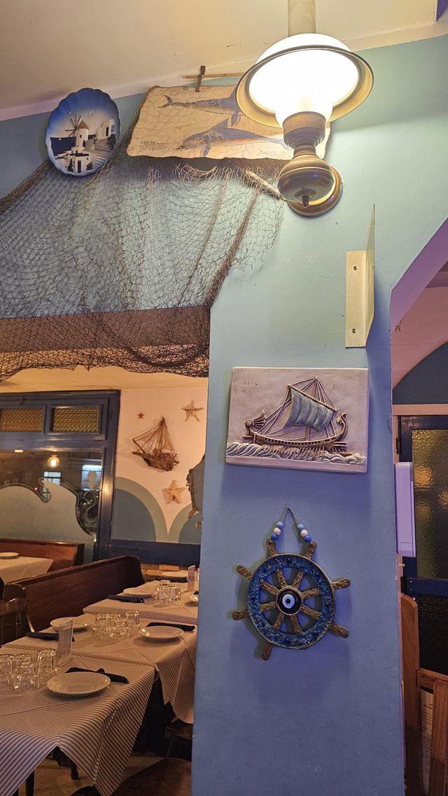 Accogliente angolo ristorante con pareti blu, decorazioni nautiche, quadri, una lampada e tavoli apparecchiati.