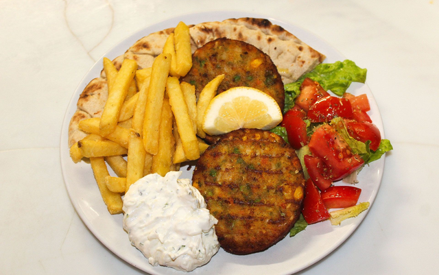 Piatto con polpette fritte, patatine fritte, pita, spicchio di limone, salsa bianca e insalata di pomodori.