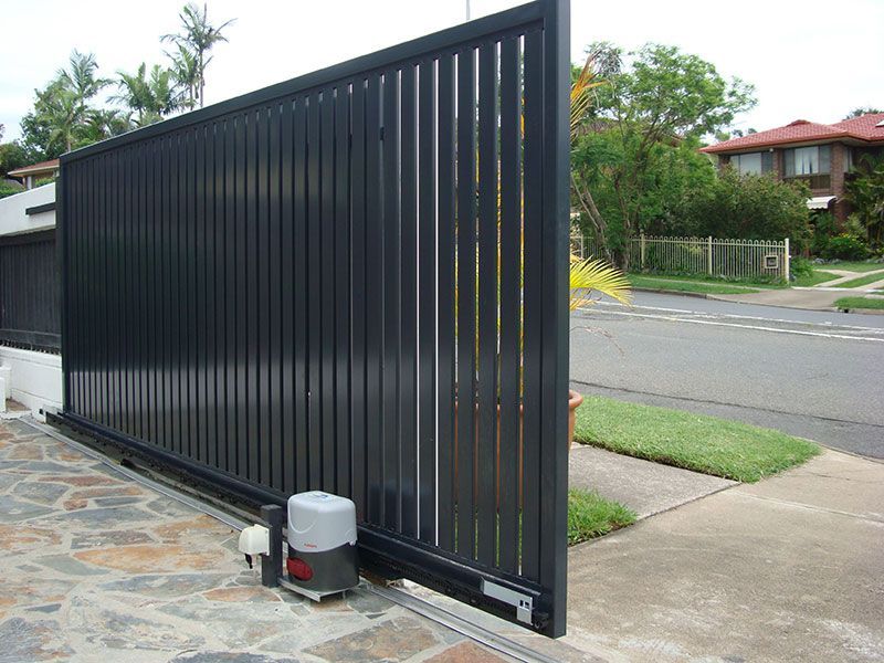 Dark gray sliding gate opening, revealing street and houses. Motorized mechanism visible.