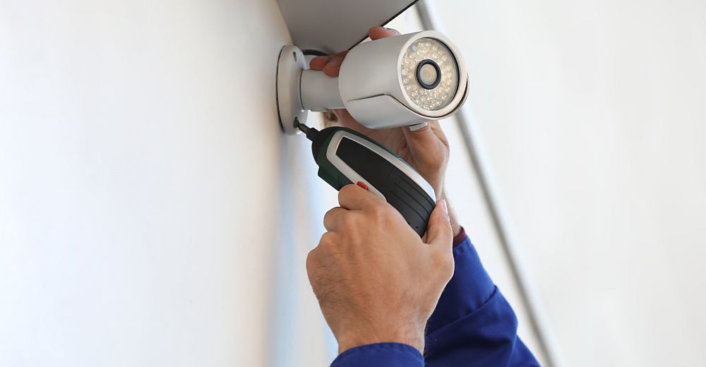 Person using a screwdriver to install a white security camera on a wall.