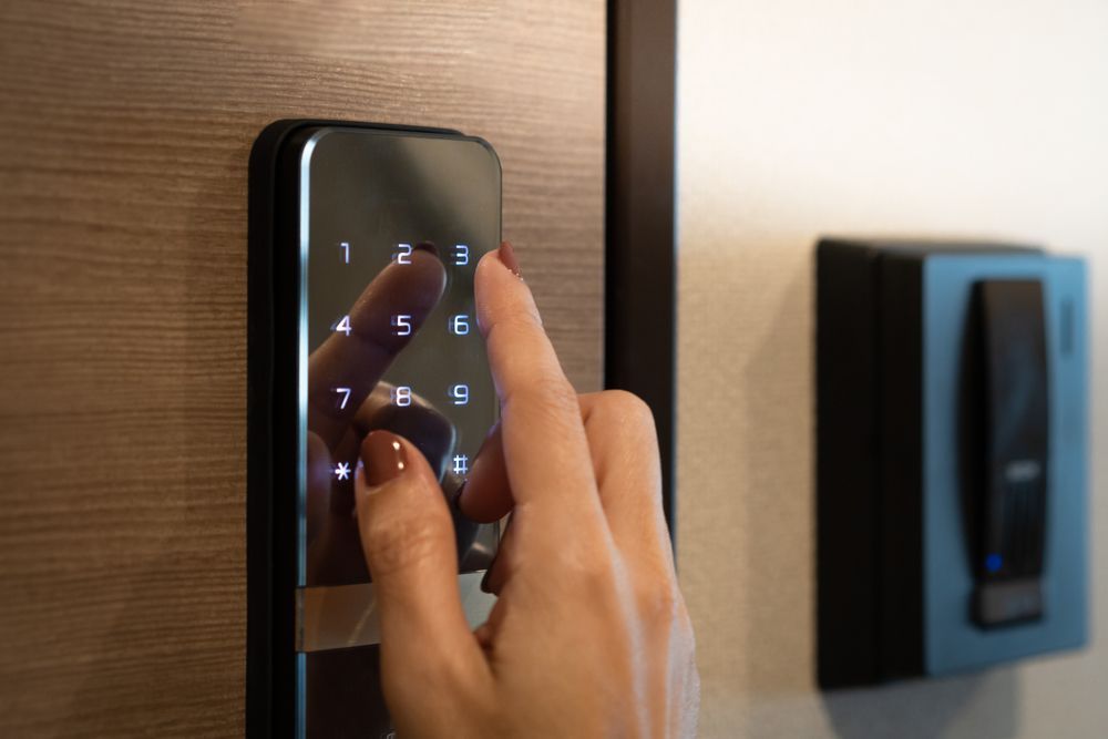A person's hand is entering code on                           
a digital keypad door lock; a card 
reader is mounted nearby on the  
wall.
