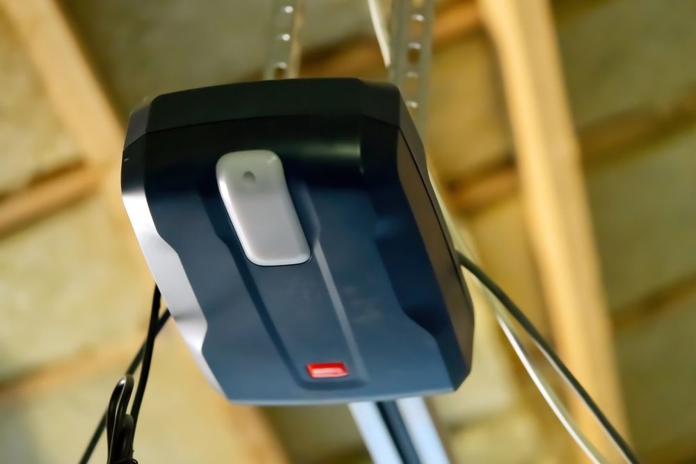 Garage door opener, black and gray unit with red light, mounted on ceiling.