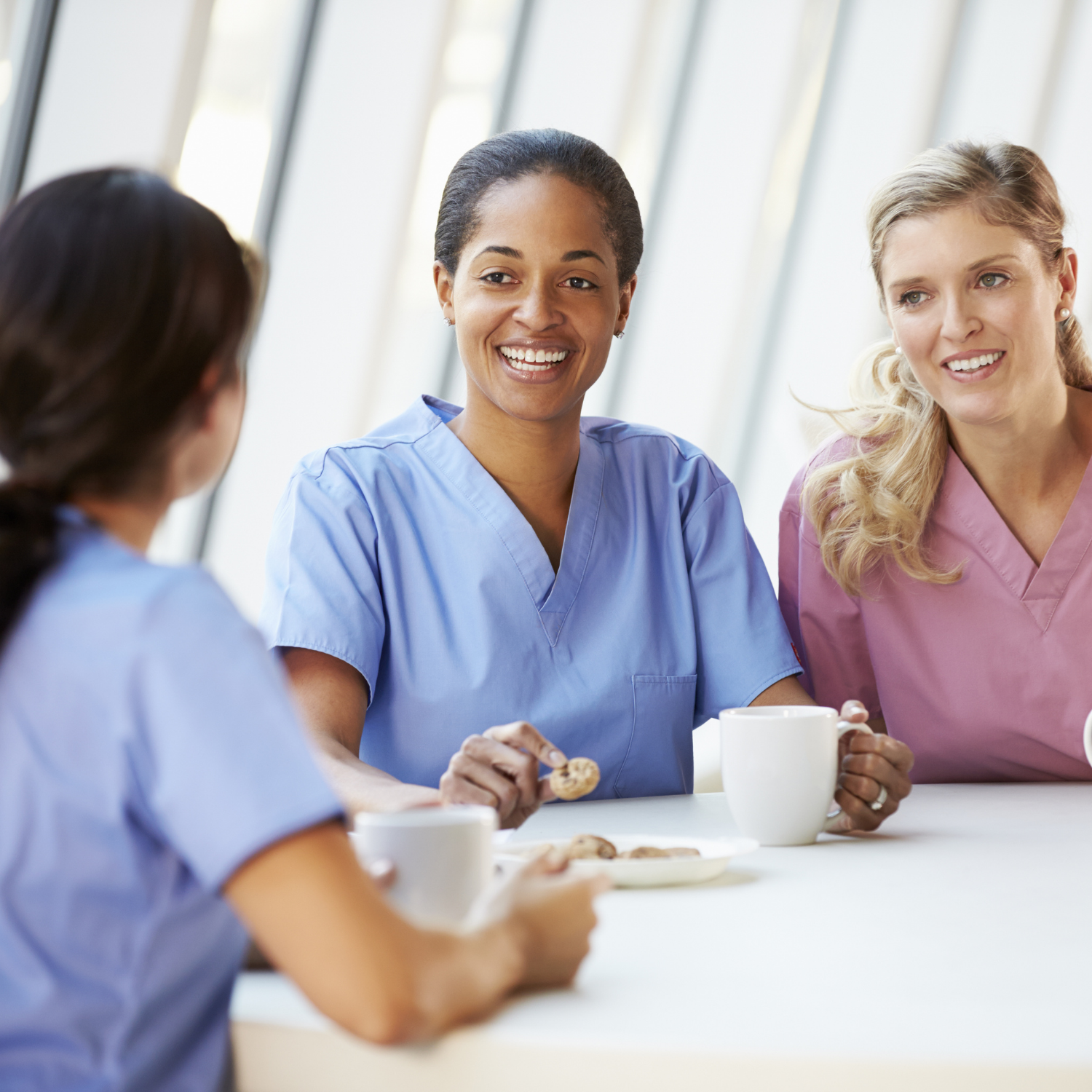 Three nurses are sitting at a table with cups of coffee