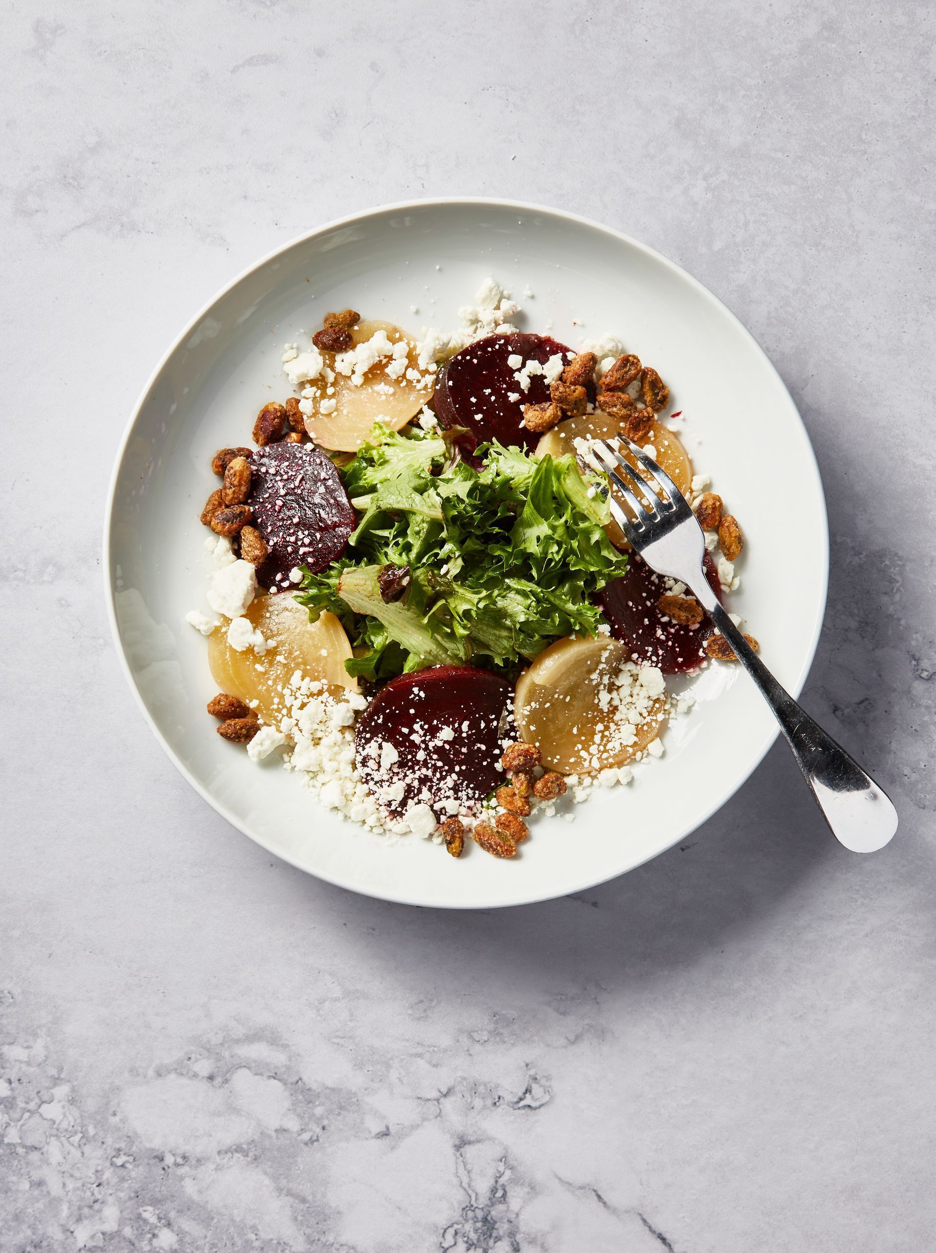 Salad with roasted beets, goat cheese, and walnuts on a white plate with a fork.