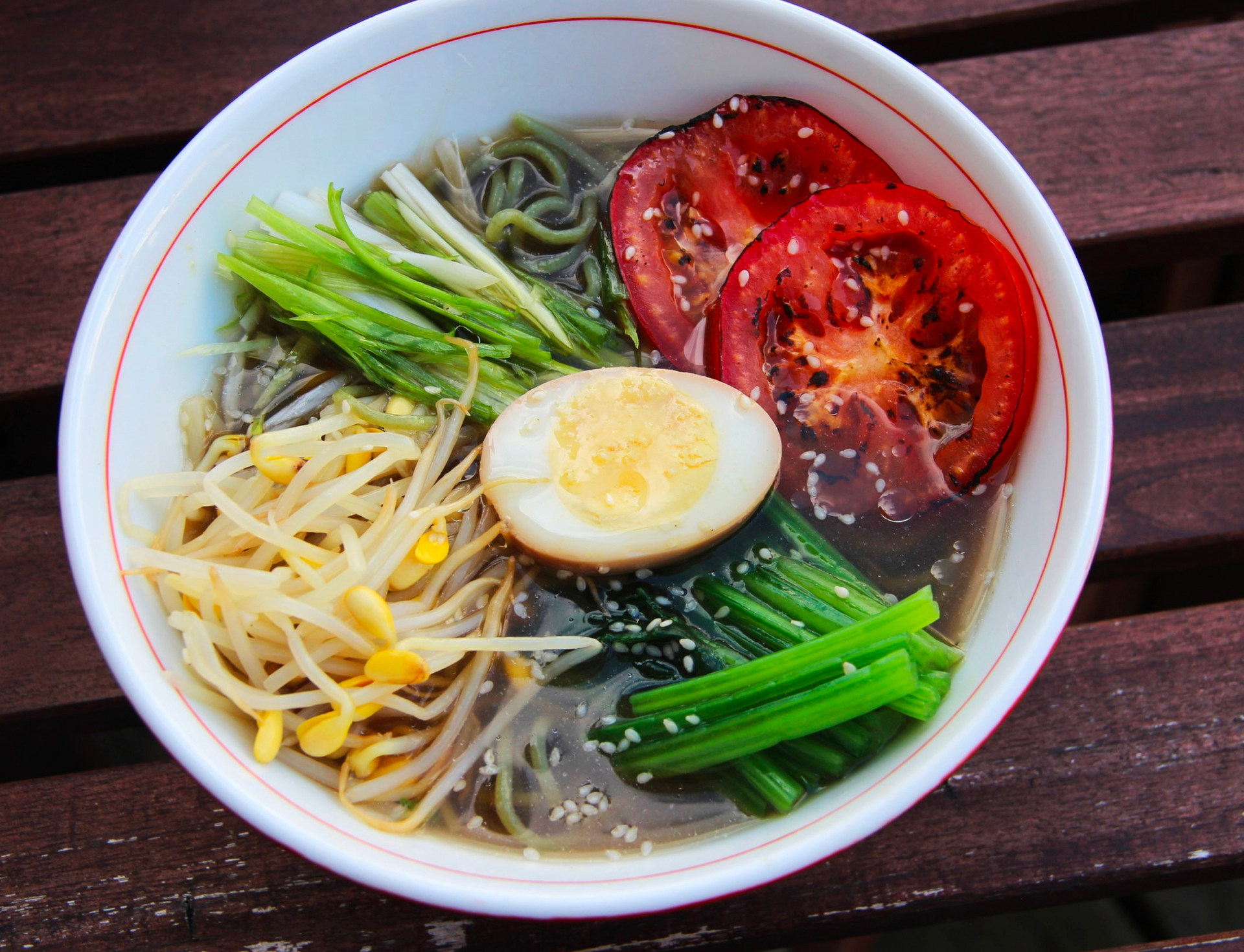 Bowl of ramen with noodles, egg, tomatoes, bean sprouts, and greens.