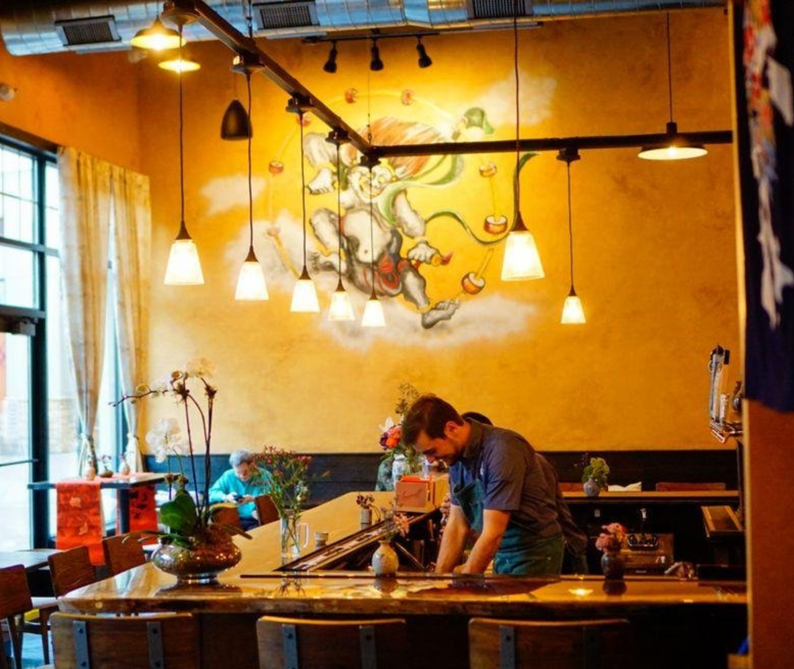 A person working behind a bar in a restaurant with a mural on the wall.